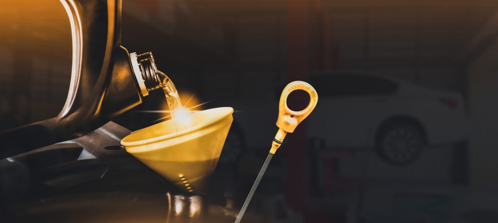 A close-up of engine oil being poured into a funnel with a car's dipstick visible in the background.