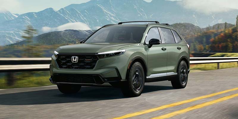 Green Honda Vehicle driving on a scenic road with mountains in the background.