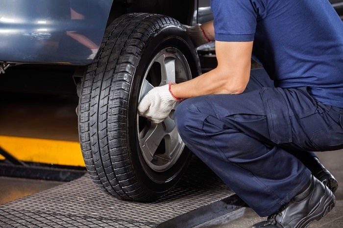 A mechanic replacing a tire on a vehicle, kneeling down and working with the wheel in a workshop setting.