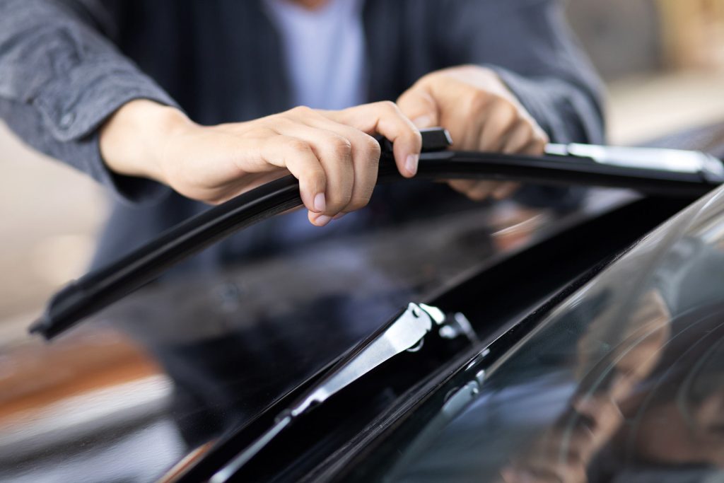 Person replacing windshield wiper blades on a car.