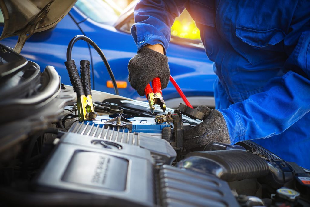 Mechanic connecting jumper cables to car battery for charging or jump-start