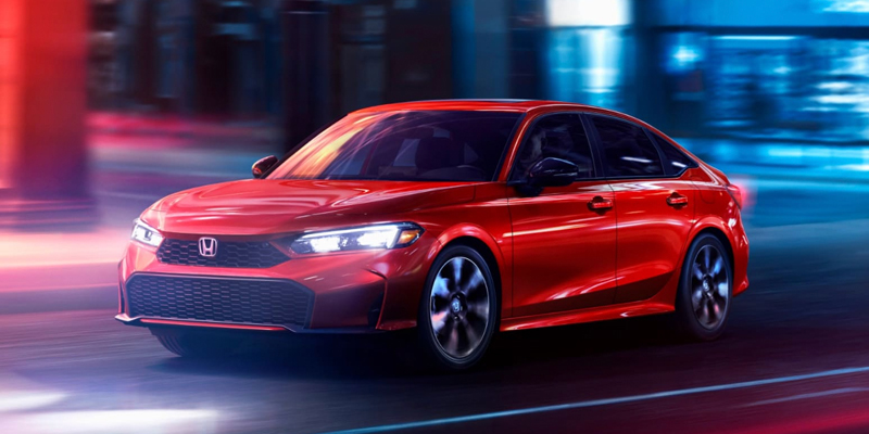 Red Honda Accord sedan driving through a city at night.