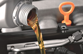 Motor oil being poured into a vehicle engine beside the dipstick.